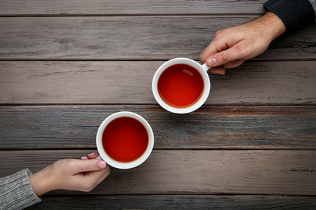 Female and male hand holding cups of tea on wooden tableの写真素材