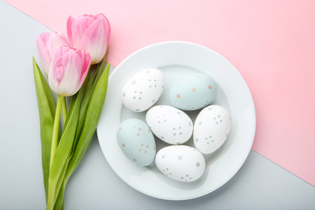 Pink tulips with easter eggs in plate on colorful backgroundの写真素材