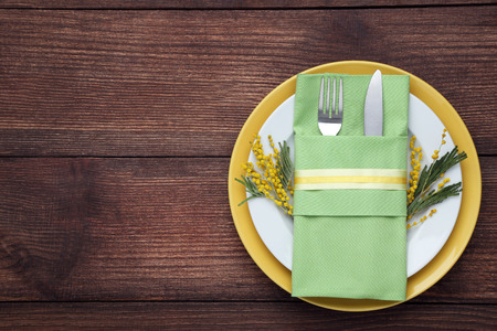 Kitchen cutlery with plate and mimosa flowers on wooden table