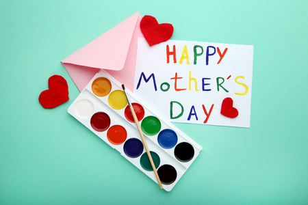 Inscription Happy Mothers Day drawn by watercolor paints with envelope and red heartsの写真素材