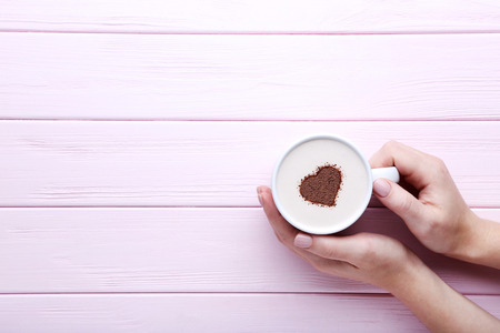 Female hands holding cup of coffee on wooden backgroundの写真素材