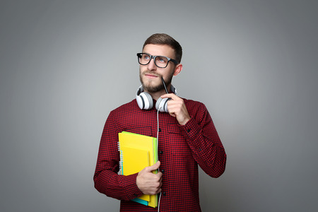 Portrait of young man with headphones and notebooks on grey backgroundの写真素材