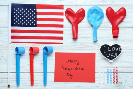 American flag, blowers, balloons and paper with inscription Happy Independence Day on wooden tableの写真素材