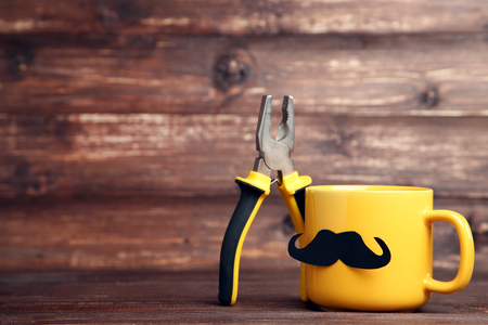 Yellow cup with pliers on brown wooden tableの写真素材
