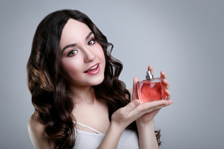 Portrait of beautiful woman with perfume bottle on grey backgroundの写真素材