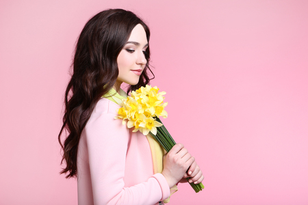 Beautiful woman in fashion clothes with narcissus flowers on pink backgroundの写真素材