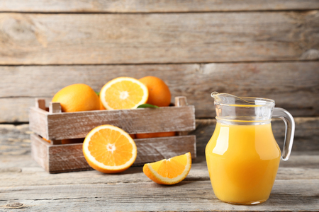 Orange fruit in crate with jug of juice on grey wooden tableの写真素材