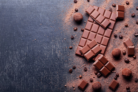 Chocolate pieces with coffee beans and cocoa powder on wooden table