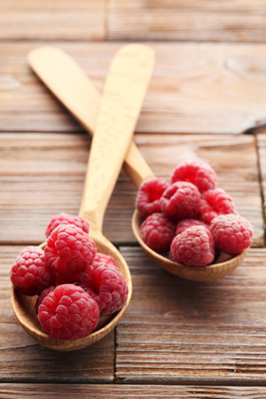 Ripe raspberries in spoons on brown wooden tableの写真素材