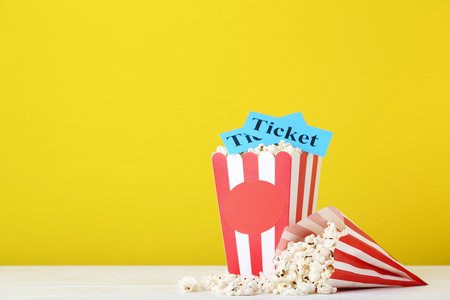 Popcorn in striped bucket and paper bag on yellow backgroundの写真素材