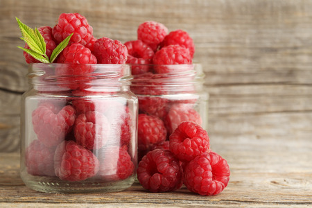 Ripe raspberries in glass jar on wooden tableの写真素材