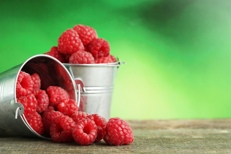 Ripe raspberries in bucket on wooden tableの写真素材