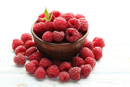 Ripe raspberries in bowl on white wooden table