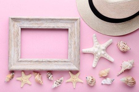 Wooden frame with seashells on pink background