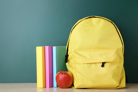 Yellow backpack with books and apple on green backgroundの写真素材