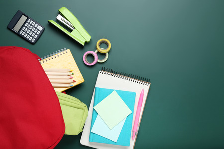 Red backpack with school supplies on green background