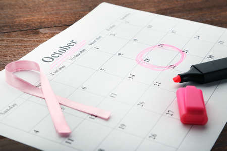 Pink ribbon with calendar sheet and marker on wooden table
