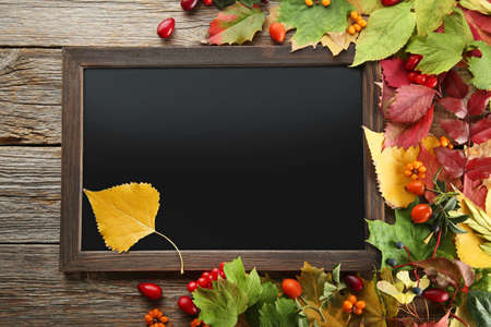 Autumn leafs with black wooden frame and berries on grey table