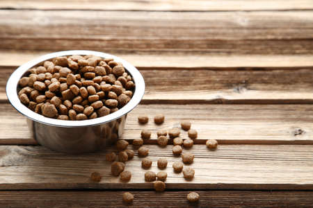 Dry cat food in bowl on wooden table