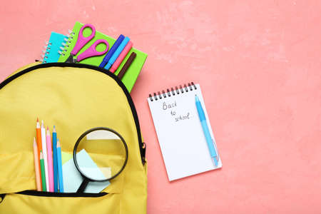 Yellow backpack with school supplies on pink background