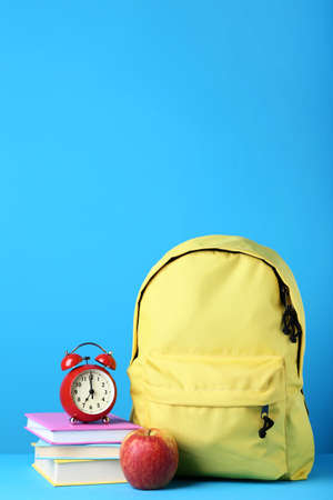 Yellow backpack with book and alarm clock on blue backgroundの写真素材