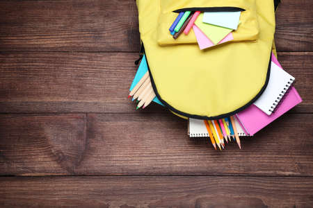 Yellow backpack with school supplies on brown wooden table