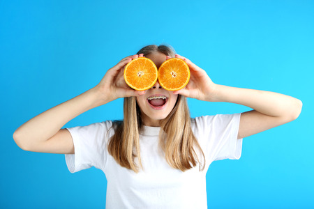 Young smiling girl with orange fruit on blue backgroundの写真素材