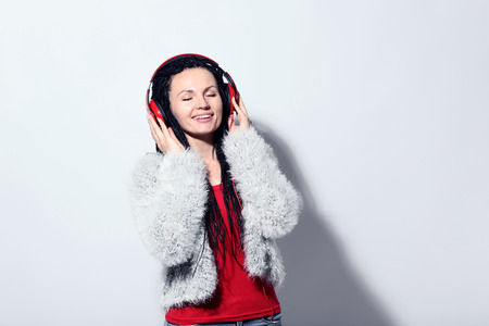 Young woman with headphones in fashion clothes on white backgroundの写真素材