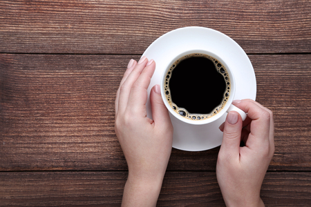 Female hands holding cup of coffee on wooden backgroundの写真素材