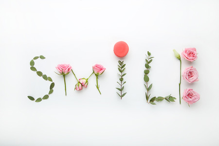Inscription Smile by flowers and green leafs on white backgroundの写真素材