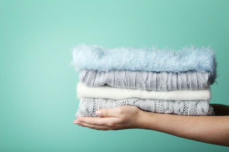 Female hands holding stack of knitted sweaters
