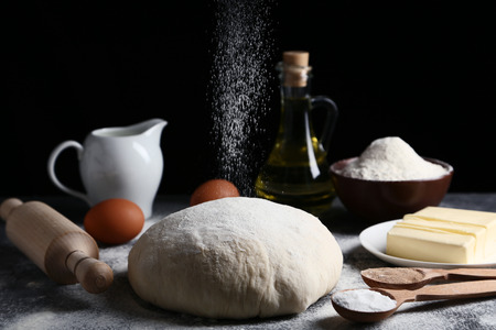 Raw dough with butter in plate, eggs and rolling pin on wooden table