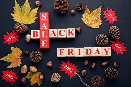 Red sale tags with wooden cubes, cones and dry leafs on black backgroundの写真素材