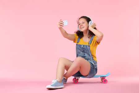 Young girl making selfie and sitting on skateboardの写真素材