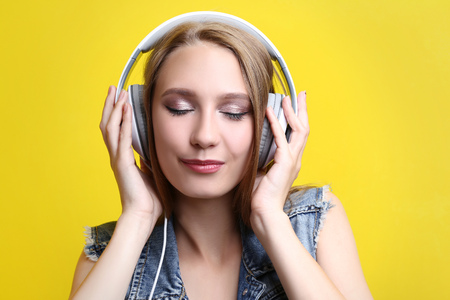 Young woman with headphones on yellow backgroundの写真素材