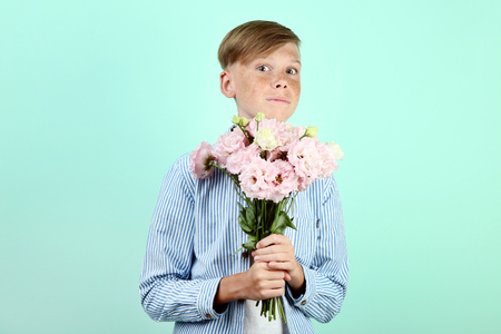 Beautiful young boy with eustoma flowers on mint backgroundの写真素材