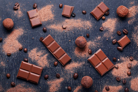 Chocolate pieces with coffee beans and cocoa powder on wooden table