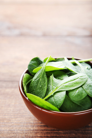 Spinach leafs in bowl on brown wooden tableの写真素材
