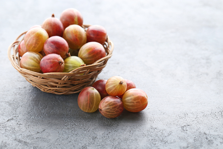 Ripe gooseberries fruit in basket on grey wooden tableの写真素材