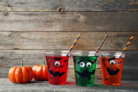 Halloween cocktail in plastic cups with pumpkins on grey wooden tableの写真素材