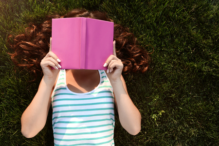 Young woman with book lying on green grass in the parkの写真素材