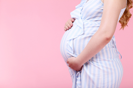 Pregnant woman in striped dress on pink backgroundの写真素材