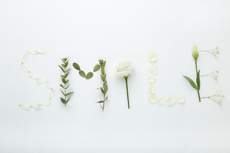 Inscription Smile by flowers and green leafs on white background