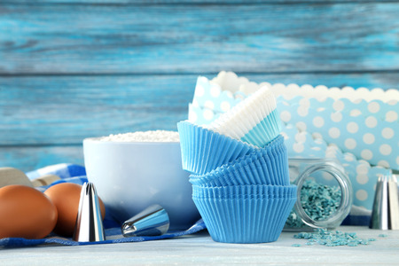 Empty cupcake cases with bowl of flour and eggs on wooden table