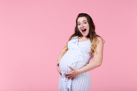 Beautiful pregnant woman in striped dress on pink backgroundの写真素材