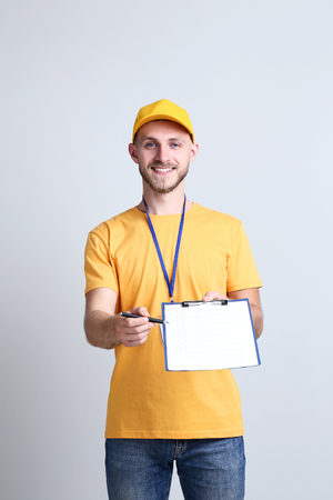 Delivery man in yellow uniform with clipboard on grey backgroundの写真素材
