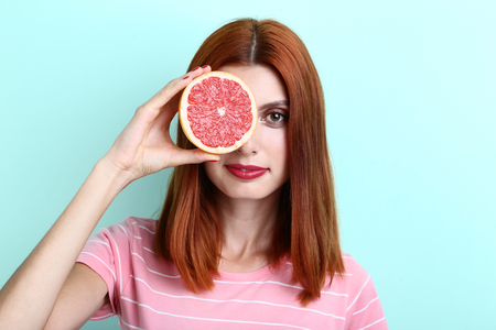 Young redhaired woman with grapefruit on mint backgroundの写真素材