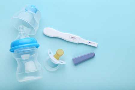 Pregnancy test with pacifier and little bottle on blue background