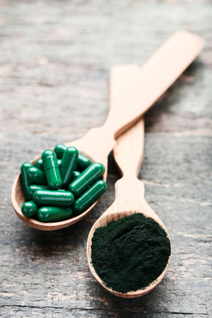 Spirulina powder and capsules in spoons on wooden tableの写真素材