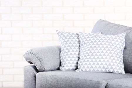 Modern grey sofa with pillows on brick wall background